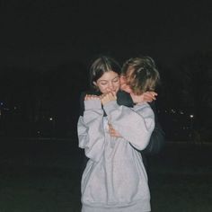 two people standing in the grass with their arms around each other and one person covering his face