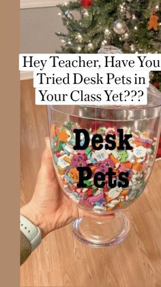 a person holding up a glass bowl filled with lots of colorful buttons and the words desk pets in front of a christmas tree