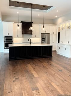 an empty kitchen with wood floors and white cabinets in the center, along with black appliances