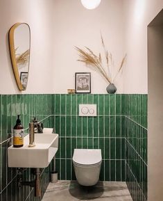 a green tiled bathroom with a toilet, sink and mirror on the wall next to it