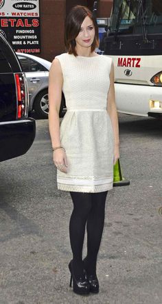 a woman standing in front of a bus wearing a white dress and black tights