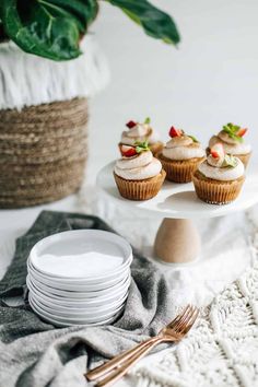 cupcakes with strawberries on top are sitting on a plate next to plates