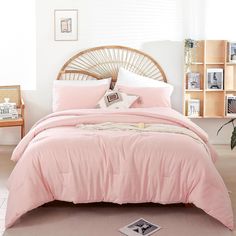 a bed with pink comforter and pillows in a room next to a plant on the floor