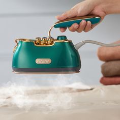 a person is holding a teal purse with steam coming out of it and the handle has gold accents