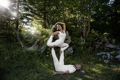 two people are doing yoga in the grass near some rocks and trees, while one person is holding his head up