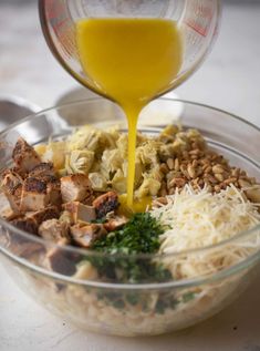 someone pouring orange juice into a bowl filled with pasta and meats, nuts, parmesan cheese, and other ingredients