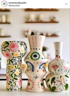 three vases are sitting on a table with flowers and leaves painted on the sides