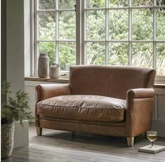 a brown leather chair sitting in front of a window next to a potted plant