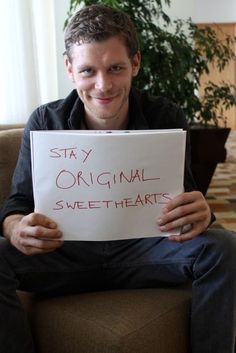 a man sitting in a chair holding a sign that says stay original sweet - hearts