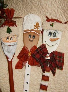 three wooden spoons decorated like santa claus, snowman and elf faces on a white quilt