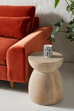 an orange couch sitting next to a table with a vase on it and a plant in the corner