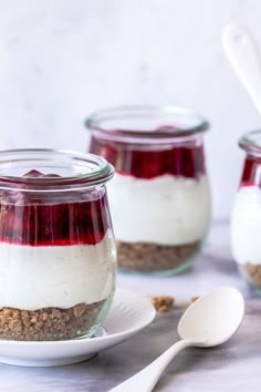 three jars filled with dessert sitting on top of a white plate next to spoons