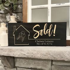 a wooden sign that says sold with a house and key on it next to vases