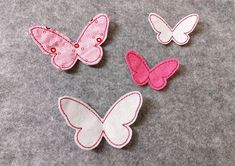 three pink and one white butterfly appliques on a gray surface with grey felt