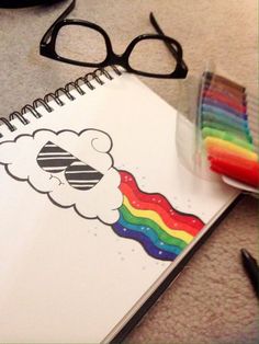 a spiral notebook with a rainbow and clouds on it next to some colored crayons