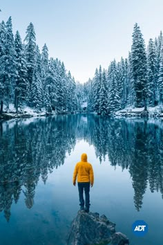 a person standing on a rock in front of a lake surrounded by snow covered trees