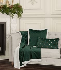 a white couch sitting next to a fireplace covered in green blankets and christmas decorations on top of it