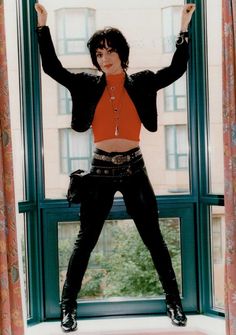 a woman standing in front of a window with her arms up and legs crossed, wearing black