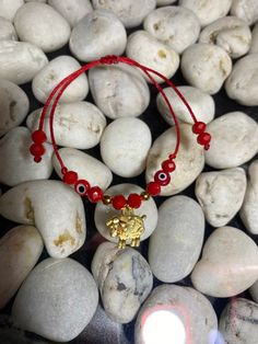 a red beaded bracelet with an evil eye charm sits on top of some rocks