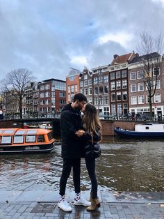 a man and woman standing next to each other in front of some buildings on the water