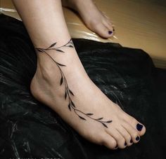 a woman's foot with leaves tattoo on the bottom of her left leg and black toenails