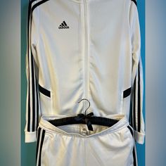 The Adidas White Tracksuit Exudes Classic Sporty Sophistication With A Clean, Crisp Aesthetic. This Ensemble Features A Sleek, Zip-Up Jacket With A Streamlined Design, Typically Accented By The Iconic Three-Stripe Detailing Running Down The Sleeves. The Matching Pants Offer A Tailored Fit With An Elastic Waistband And Tapered Legs For A Modern, Flattering Silhouette. Crafted From High-Quality, Breathable Fabric, The Tracksuit Provides Both Comfort And Durability, Making It Ideal For Workouts Or White Tracksuit, Adidas Track Suit, Adidas Pants, White Adidas, Athletic Wear, Matching Sets, Adidas Women, Breathable Fabric, Zip Ups