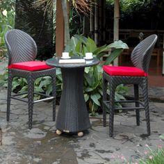 three chairs and a table with red cushions on it in front of some greenery