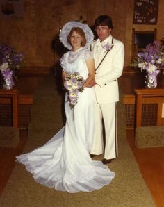 a man and woman standing next to each other in front of a table with flowers