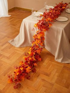 the table is set with white plates and place settings, along with an orange vine