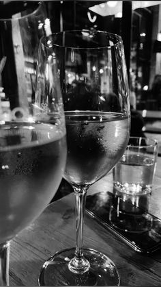 two wine glasses sitting on top of a wooden table next to another glass filled with liquid