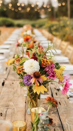 a long wooden table topped with vases filled with flowers next to glasses and candles