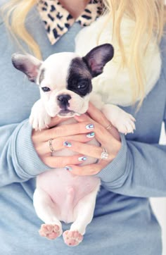 a woman holding a small dog in her arms while wearing blue and white nail polish