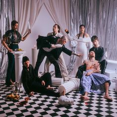 a group of people standing and sitting on top of a black and white checkered floor