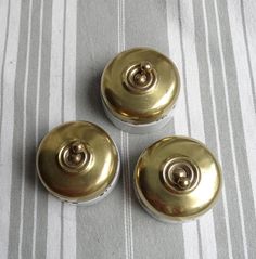 three metal knobs sitting on top of a white and gray striped table cloth next to each other