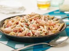 a skillet filled with pasta and meat on top of a blue table cloth next to silverware