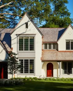 a large white house with red doors and windows in the front yard, on a sunny day