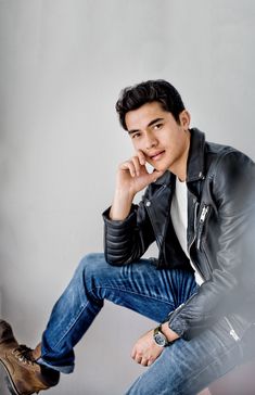 a young man sitting on top of a chair wearing a black leather jacket and jeans