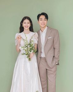 a man and woman standing next to each other in front of a green wall holding flowers