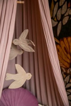 two doves hanging from a string in front of pink drapes with curtains behind them