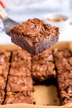 a person holding a piece of chocolate brownie over a pan full of brownies