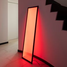 a red light shining on the floor next to a white wall and some stairs in an office building