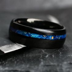 a black ring with blue and gold inlays sits next to a knife on a table