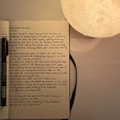 an open notebook with writing on it next to a lamp