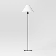 a black floor lamp with a white shade on the top and bottom, against a gray background