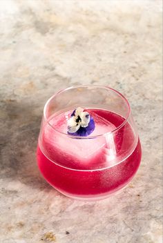 a pink drink in a glass with a flower on the top, sitting on a marble surface