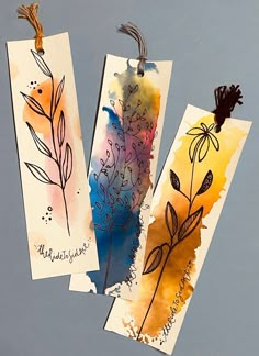 three bookmarks with watercolor designs on them hanging from clothes pins and paper clips