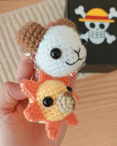 a hand holding two small crocheted animal keychains in front of a book