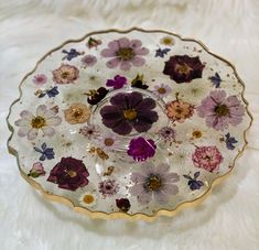 a glass plate with flowers on it sitting on a white cloth covered tablecloth,