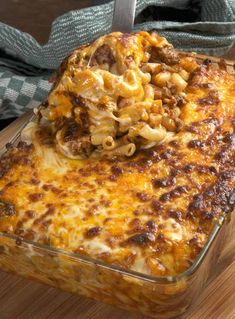 a casserole dish with pasta and meat in it on a wooden table next to a fork