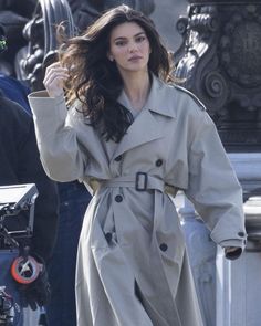 a woman in a trench coat walking down the street